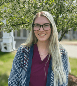 Outdoor portrait of Madison Scampini, RN, BSN, smiling in front of greenery at Holden Rehabilitation & Skilled Nursing Center.