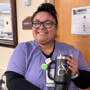 Adriana Rivera, LPN at Oakdale Rehabilitation & Skilled Nursing Center, smiling in uniform while holding a branded Oriol Health Care mug.