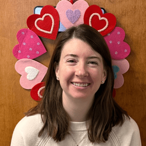 Hayley Lyon, HR and Finance Coordinator at Oriol Health Care, smiling while holding a branded Oriol Health Care mug in a hallway setting.